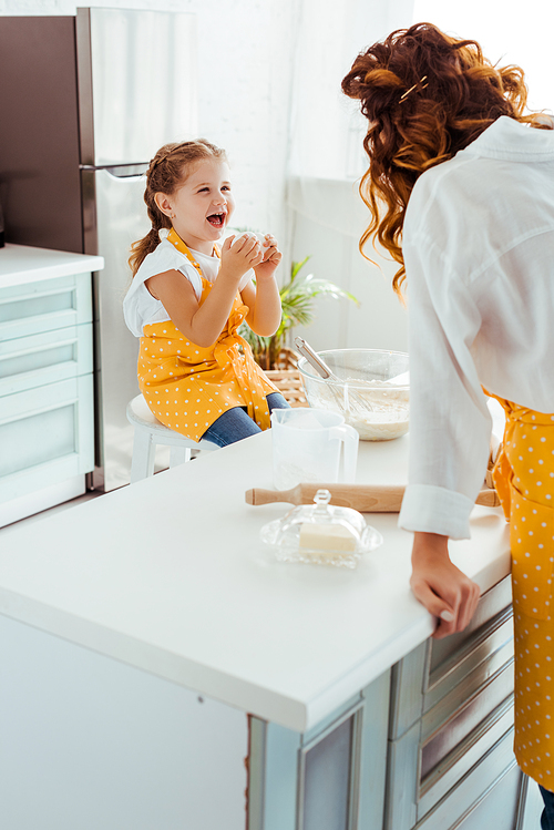 excited daughter in polka dot apron looking at mother in kitchen