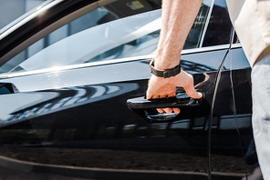 cropped view of man standing near car and touching handle while opening door