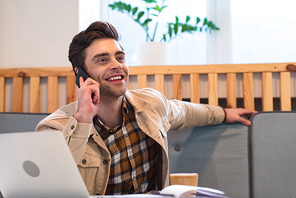 Smiling freelancer in jacket talking on smartphone in cafe