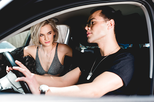 stylish handsome man and beautiful sexy girl sitting in car