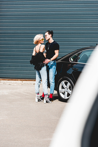 fashionable handsome man and beautiful girl posing near car