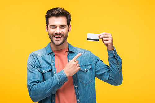 handsome man pointing with finger at credit card isolated on yellow