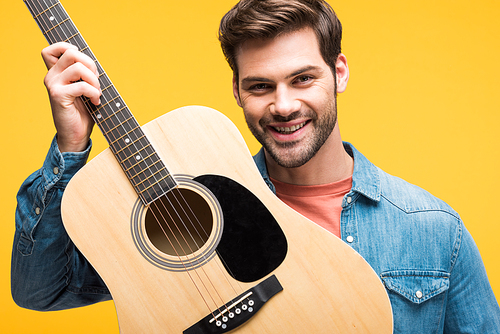 handsome happy man holding acoustic guitar Isolated On yellow