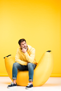 pensive man on bean bag chair touching chin on yellow