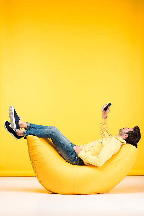 man on bean bag chair taking selfie on smartphone on yellow