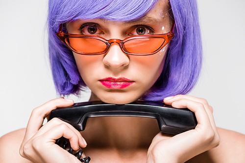 upset woman in purple wig holding retro phone, isolated on grey