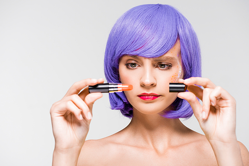 confused girl in purple wig holding lipstick isolated on grey