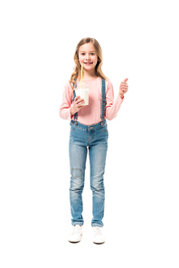 full length view of smiling kid holding milkshake and showing thumb up isolated on white