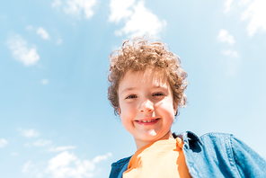 low angle view of smiling curly kid under blue sky