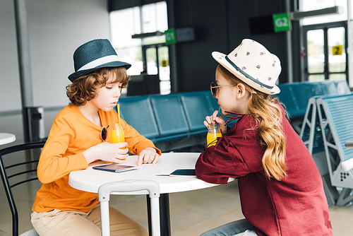 preteen kids sitting at table with orange juice in departure lounge