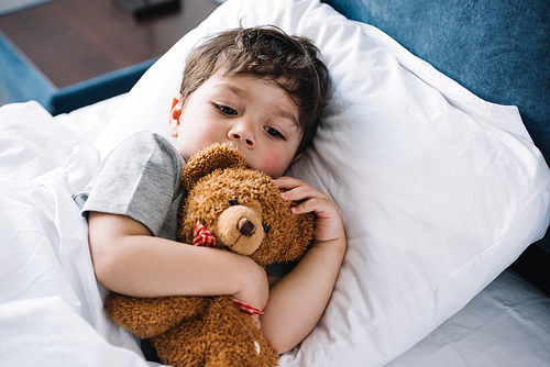 cute kid lying in bed with teddy bear at home