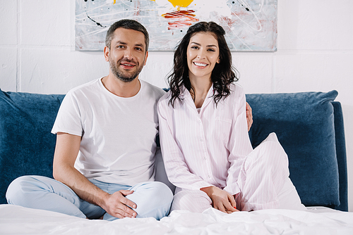cheerful man sitting near happy woman and smiling on bed