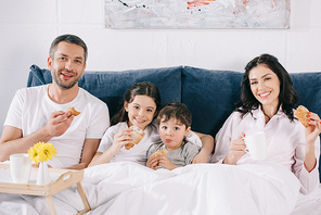 happy parents and kids holding tasty croissants in bed