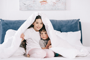 cheerful kid sitting under blanket with cute toddler brother