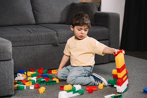 adorable toddler playing with colorful toy blocks while sitting on floor in living room
