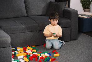 cute toddler playing with colorful toy blocks while sitting on floor in living room