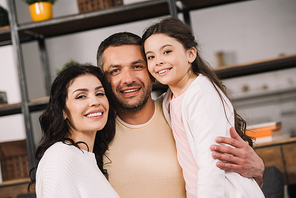 happy man hugging attractive wife and cute daughter at home