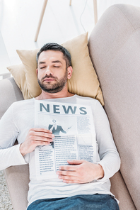 handsome bearded man with eyes closed holding newspaper and resting on couch at home