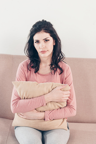 depressed woman sitting on couch,  and hugging pillow at home