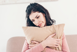 beautiful upset woman sitting and hugging pillow at home