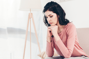 upset woman sitting on couch and propping chin with hands at home with copy space