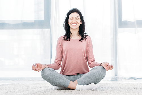 beautiful smiling woman in Lotus Pose practicing meditation in Living Room at home