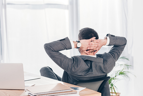 Back view of businessman with Hands Behind Back sitting at table in office