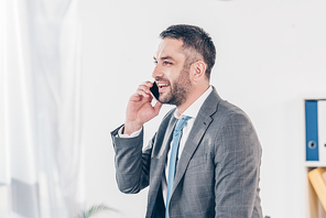 handsome smiling businessman in suit talking on smartphone in office with copy space