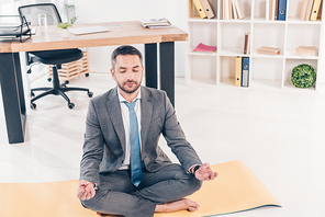 handsome businessman meditating in Lotus Pose on fitness mat in office