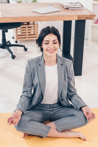 beautiful smiling businesswoman in suit meditating in Lotus Pose in office