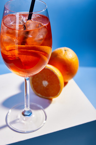 selective focus of cocktail Aperol Spritz with straw in glass and oranges on blue background