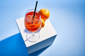 high angle view of cocktail Aperol Spritz with straw in glass and oranges on blue background