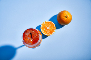 top view of cocktail Aperol Spritz with straw in glass and oranges on blue background