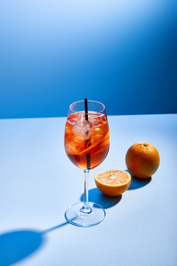 cocktail Aperol Spritz with straw in glass and oranges on blue background