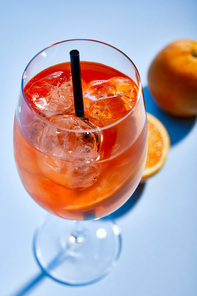 selective focus of cocktail Aperol Spritz with straw in glass and oranges on blue background
