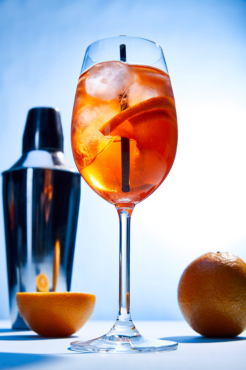 low angle view of cocktail Aperol Spritz, oranges, shaker on blue background