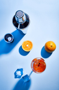 top view of cocktail Aperol Spritz, oranges, shaker, ice cubes and measuring cup on blue background