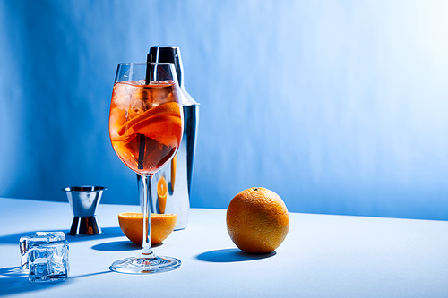 cocktail Aperol Spritz, oranges, shaker, ice cubes and measuring cup on blue background