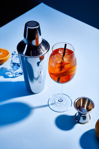 high angle view of cocktail Aperol Spritz, orange, shaker, ice cubes and measuring cup on blue background