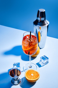 cocktail Aperol Spritz, oranges, shaker, ice cubes and measuring cup on blue background
