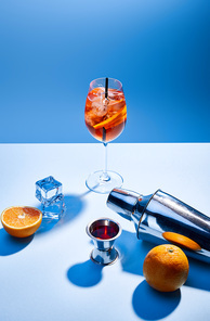 Aperol Spritz, oranges, shaker, ice cubes and measuring cup on blue background