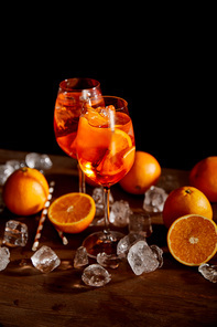 selective focus of Aperol Spritz in glasses, oranges and ice cubes on black background