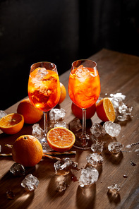 Aperol Spritz in glasses, oranges and ice cubes on black background