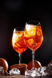Aperol Spritz in glasses, oranges and ice cubes on black background