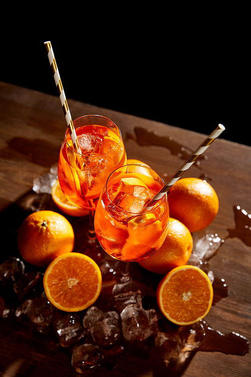 high angle view of Aperol Spritz in glasses, oranges and ice cubes on black background
