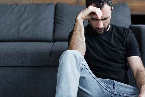 depressed handsome man in black t-shirt sitting on floor and holding hand near head