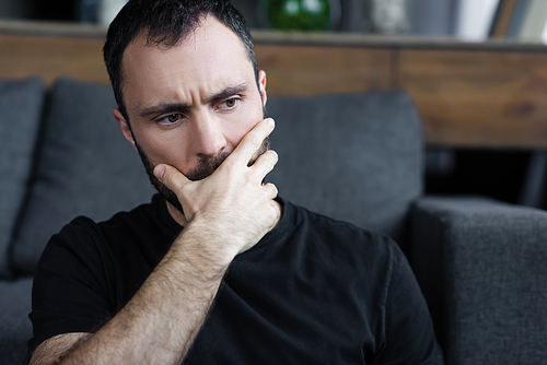 serious man in black t-shirt holding hand on on mouth while sitting at home