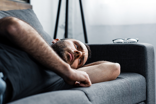 depressed man lying on grey sofa at home and looking away