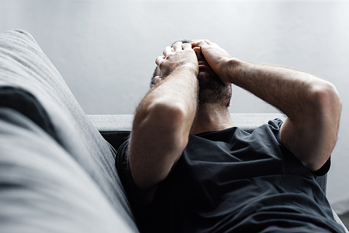 depressed man lying on sofa and suffering while holding hands on face