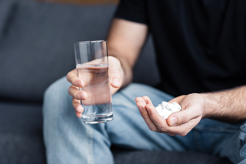 partial view of man holding glass of water and handful of drugs